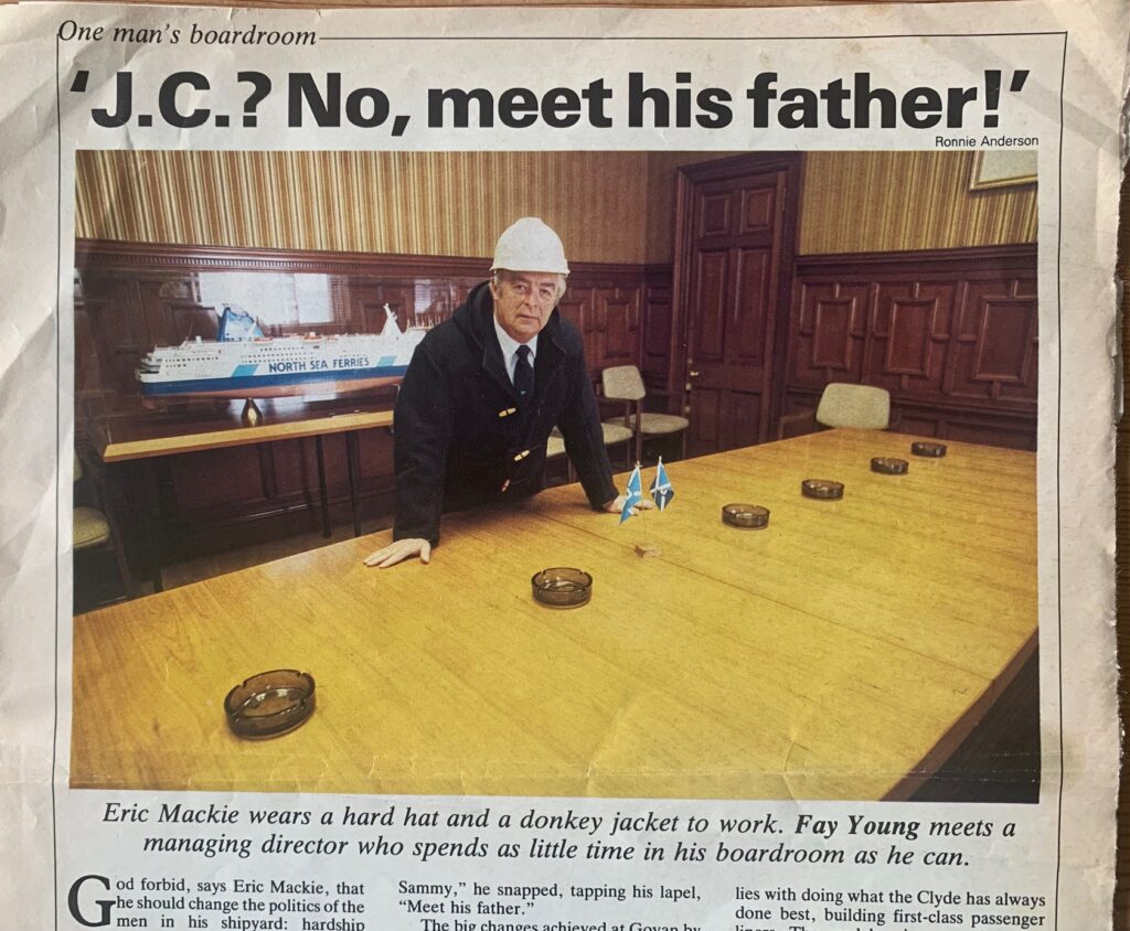 A picture of Eric Mackie managing director of Govan Shipbuilders in 1887, leaning over his boardroom table proudly sporting a hard hat